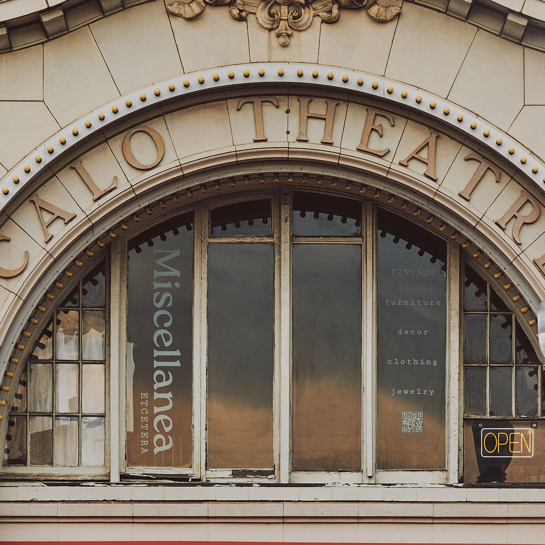 An ornate stone facade with a large arched window and raised lettering reading 'CALO THEATRE.' A vertical sign on the left window says 'Miscellanea,' and a small 'OPEN' sign is visible on the right window.