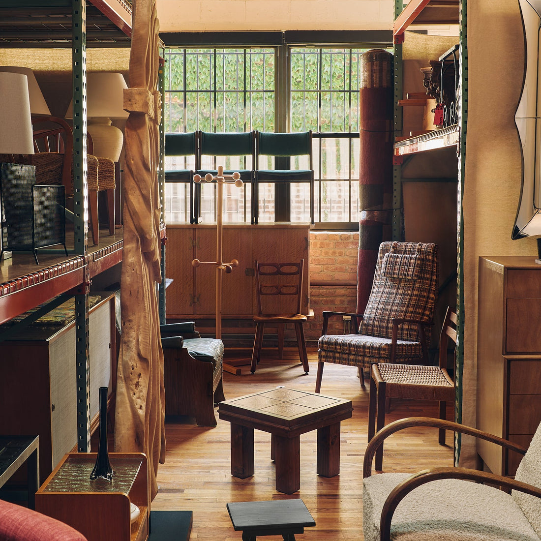 A cozy, cluttered vintage furniture showroom with wooden floors, metal shelving, and various antique chairs, tables, and lamps.