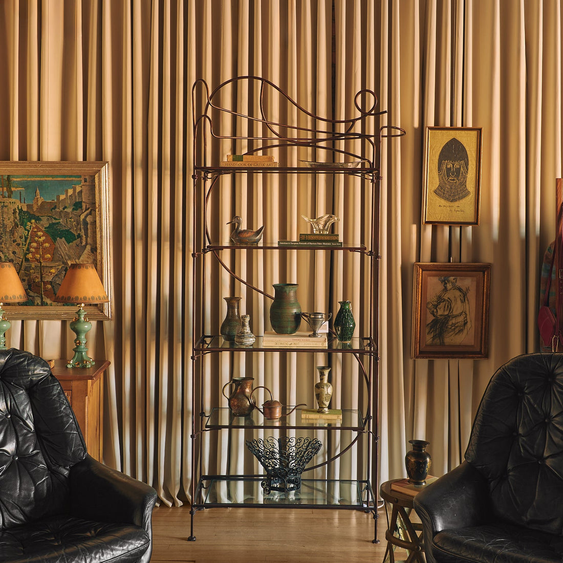 A vintage-style living room scene featuring a tall black metal five-tier shelf with glass shelves in the center, flanked by two black leather armchairs, a patterned tile floor, and a striped beige wall.